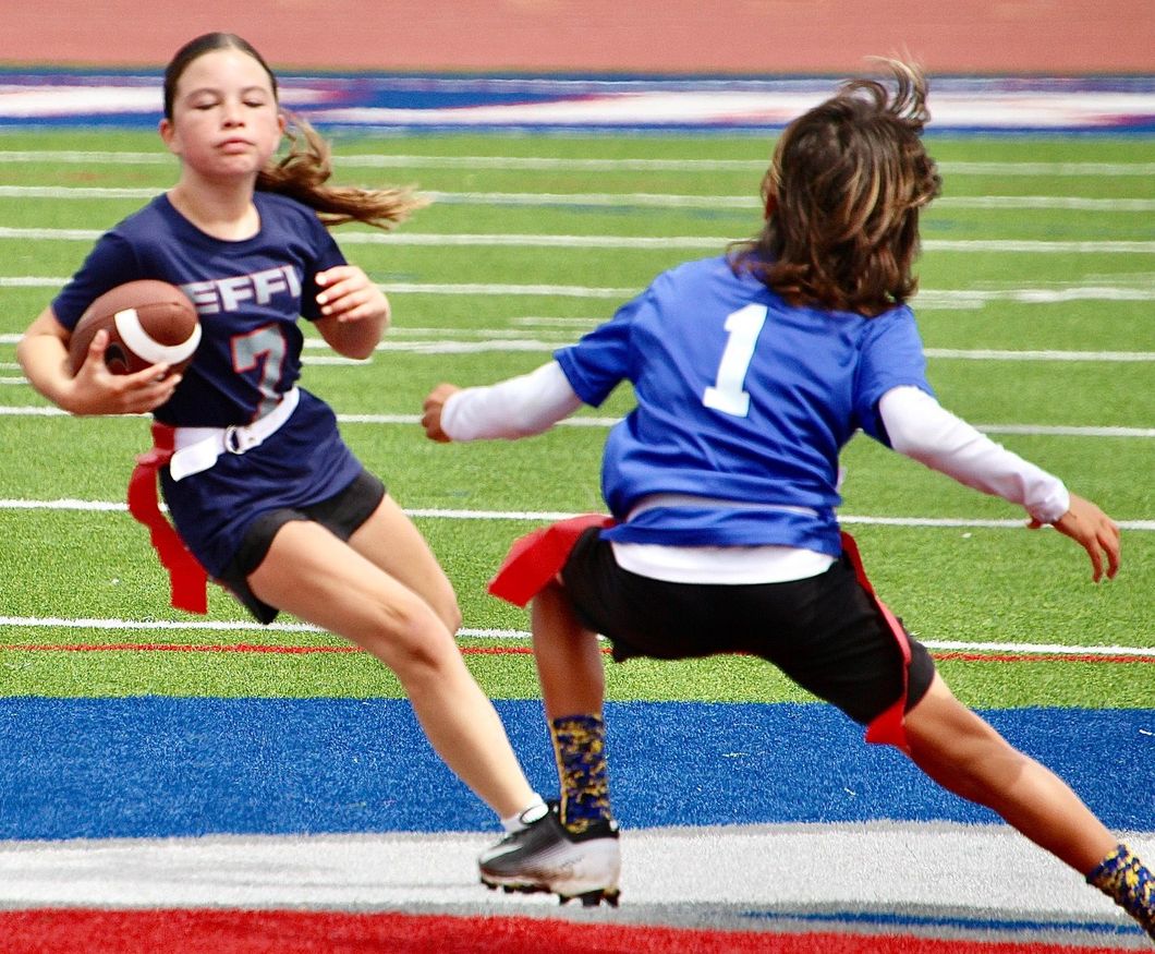 Two youth football players on a field, one running with the ball while another tries to block.