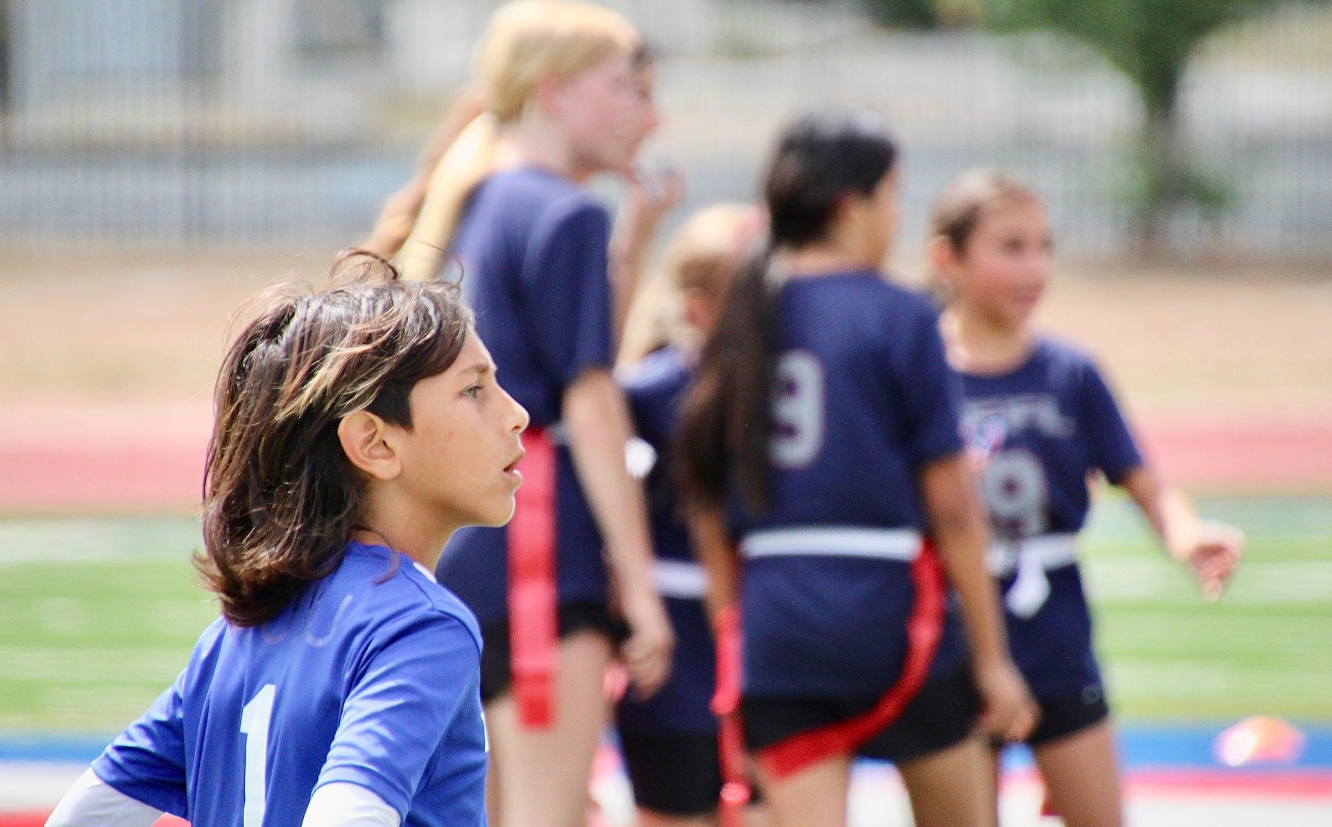 Youth soccer players in blue jerseys standing on a field, with one player in focus in the foreground