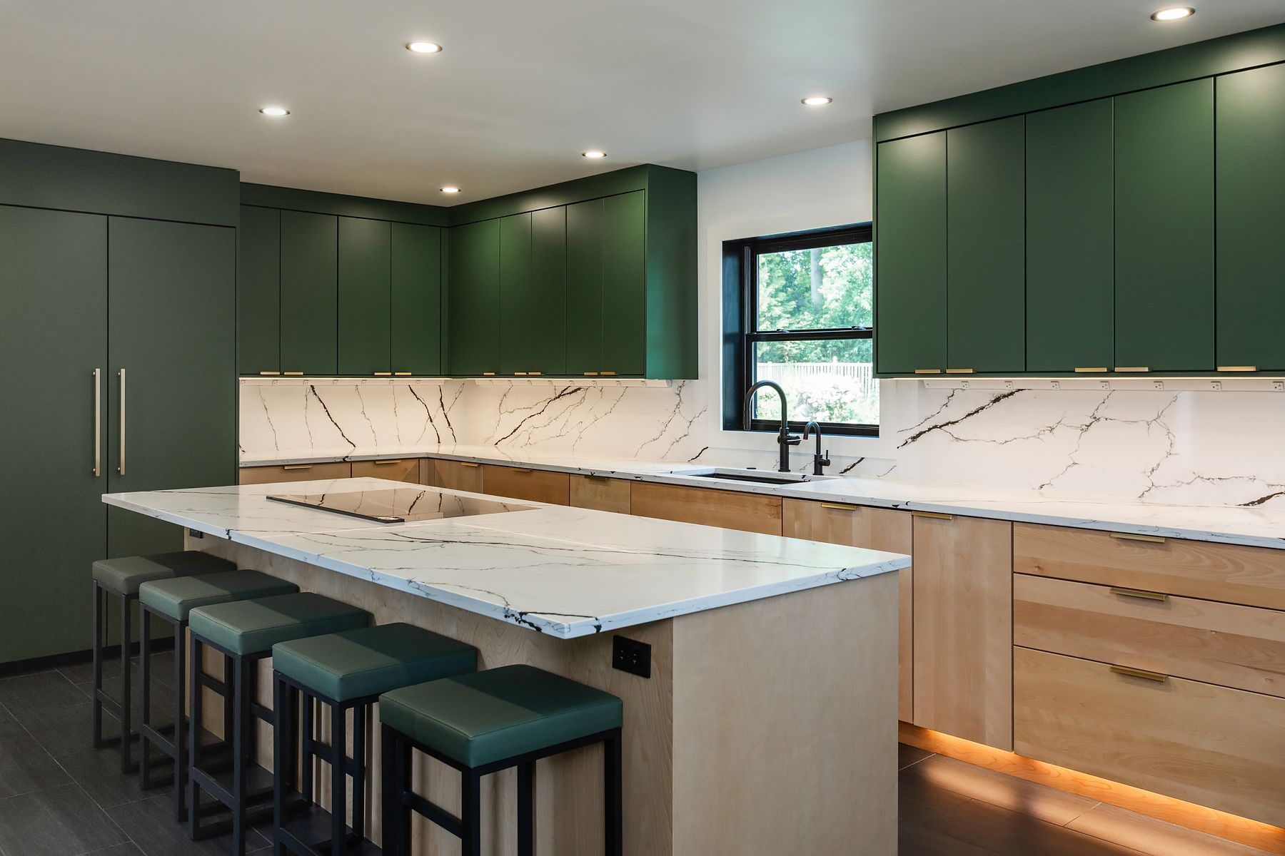 Modern kitchen with dark green cabinets, marble island, built-in benches, and recessed lighting