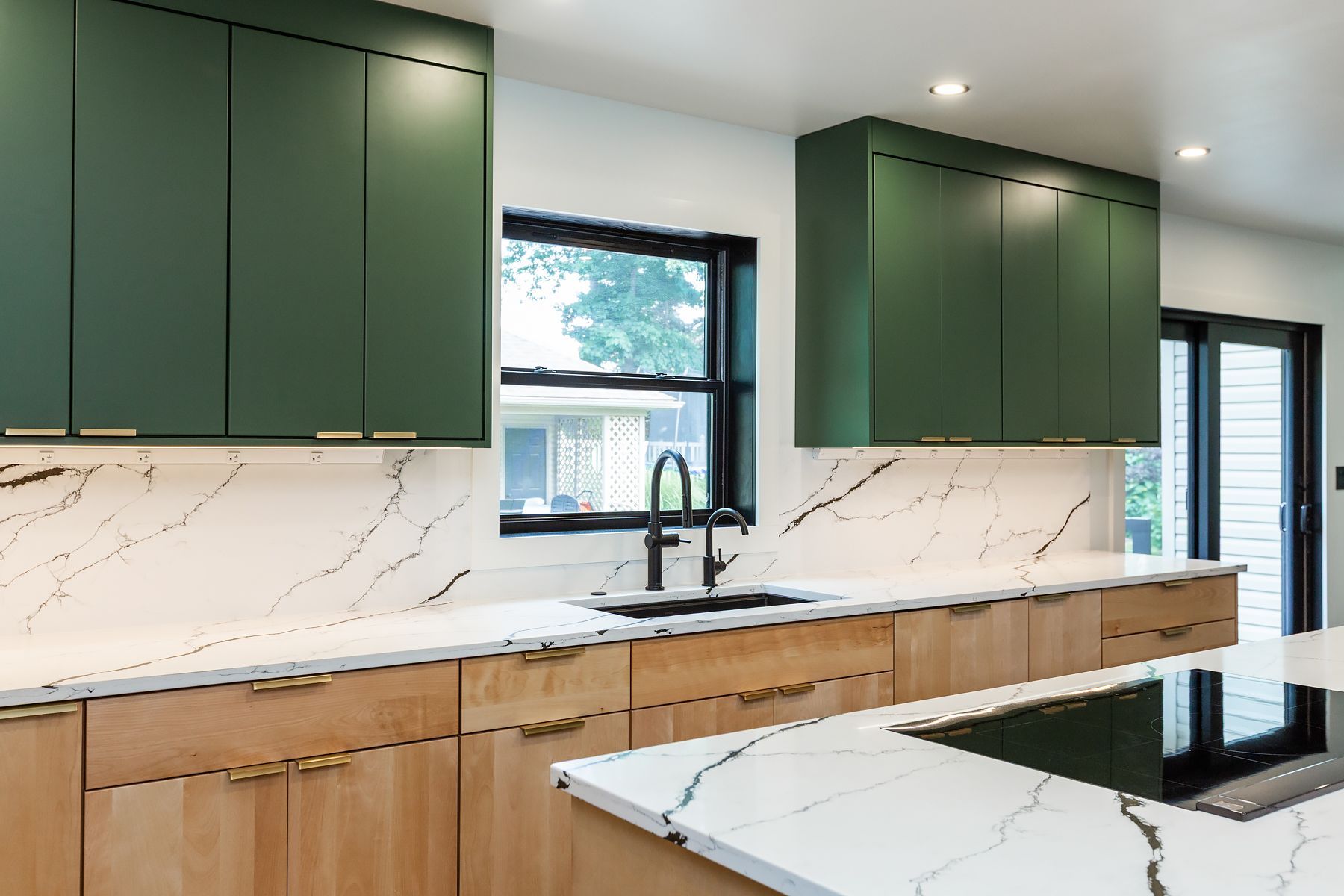 Modern kitchen with green cabinets, wood lower cabinets, white marble backsplash, and white countertops
