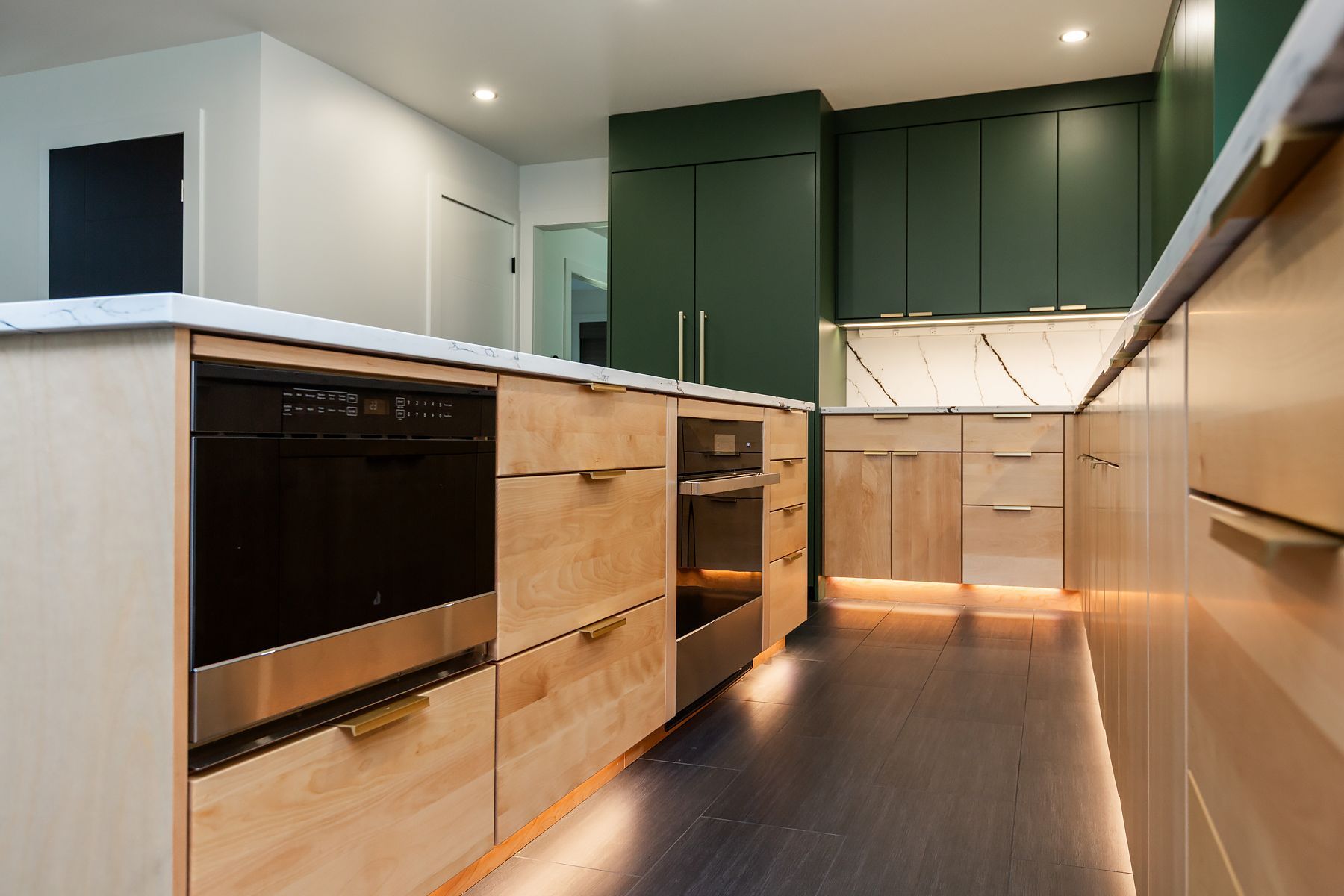 Modern kitchen with dark green cabinets, light wood cabinetry, and built-in appliances