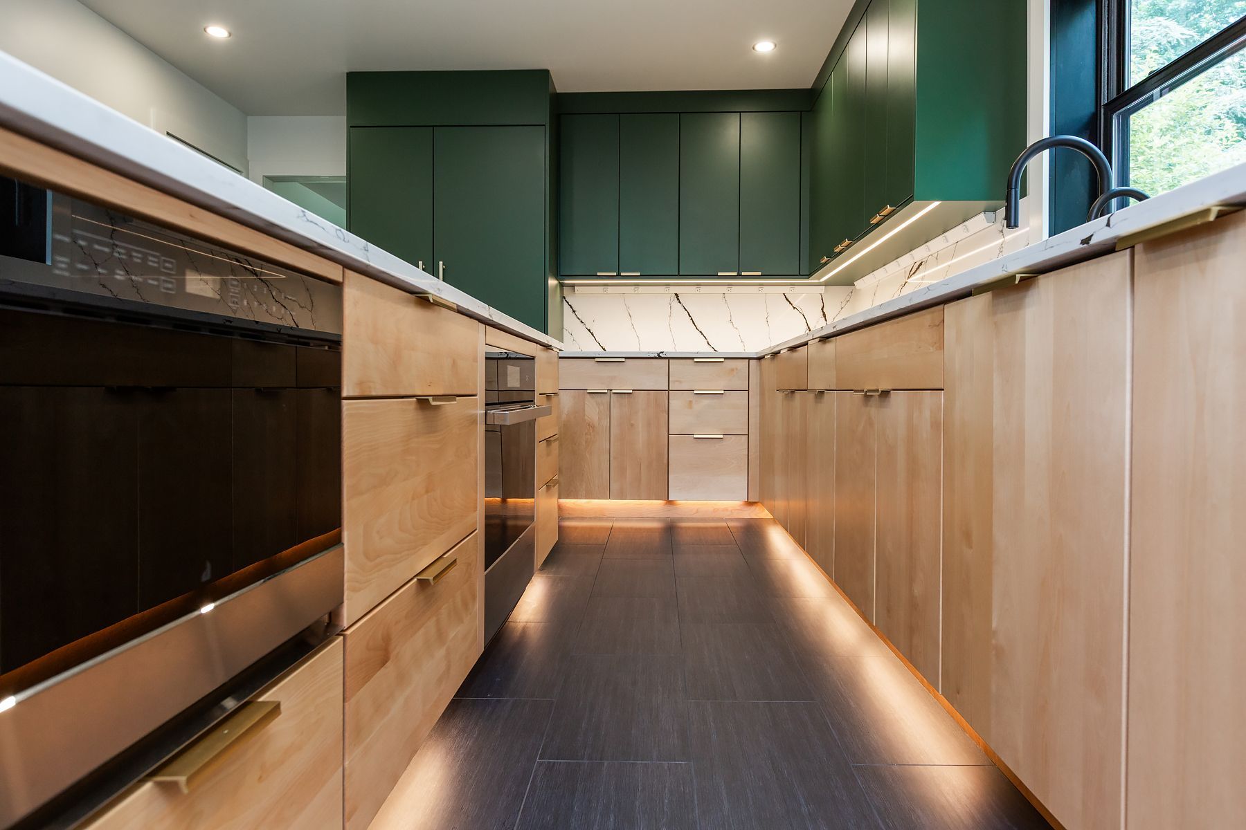 Narrow modern kitchen with green upper cabinets, wood lower cabinets, and a long counter corridor