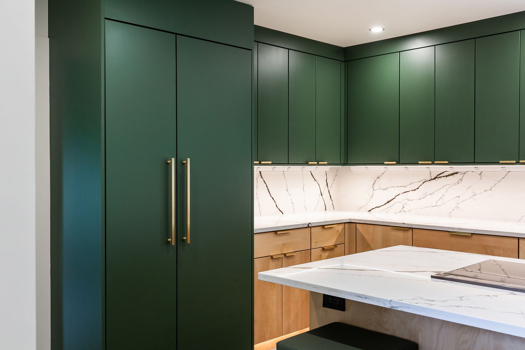 Modern kitchen with dark green cabinets, white marble backsplash, and a light stone island