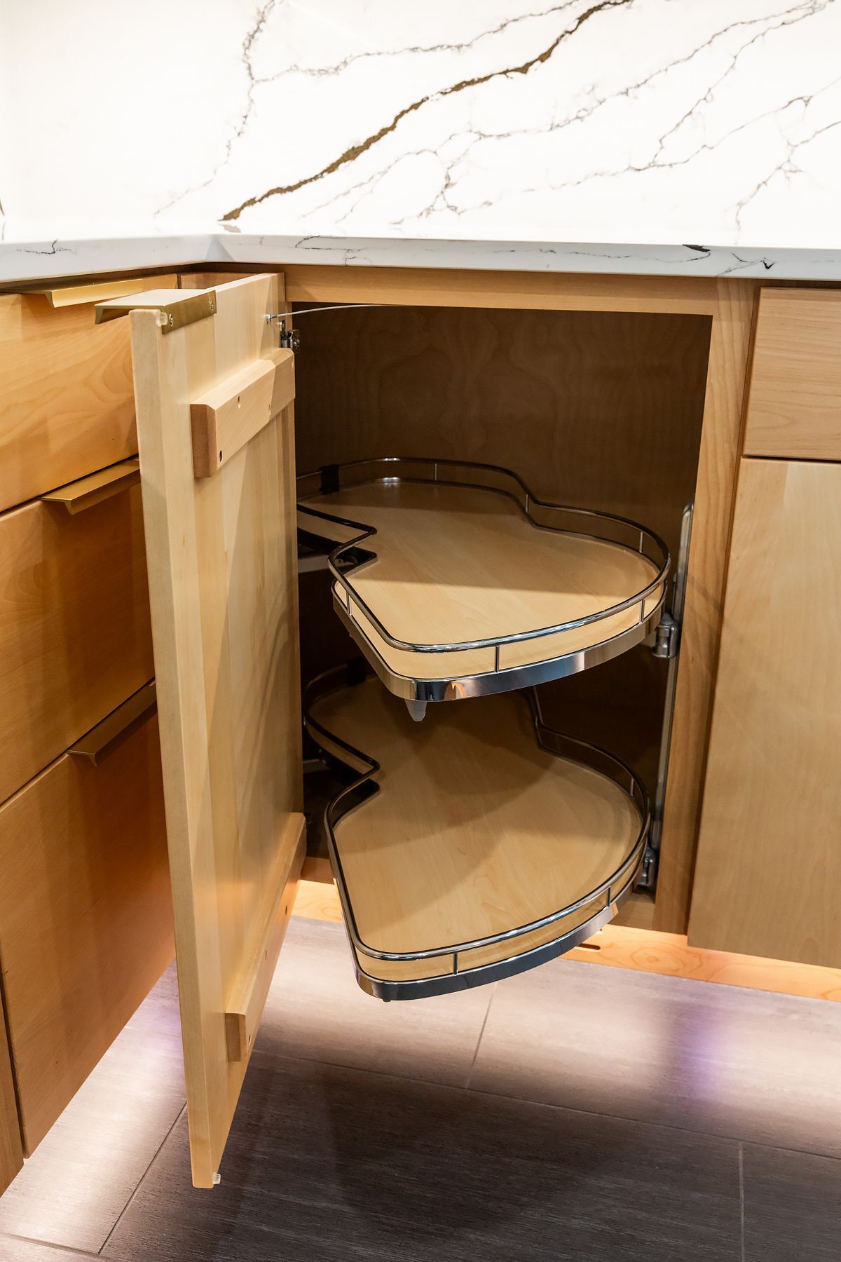 Open kitchen cabinet with pull-out corner shelves and a marble countertop above.