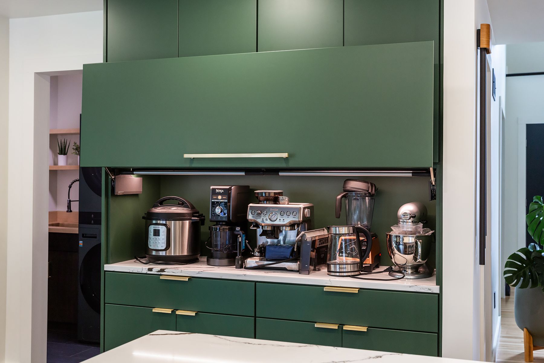Green built-in kitchen cabinet with countertop appliances and mugs displayed on shelves