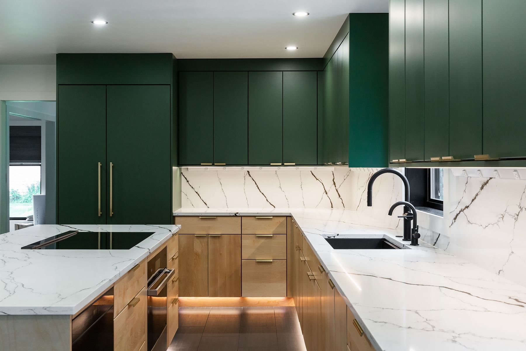 Modern kitchen with dark green cabinets, marble countertops, and brass handles