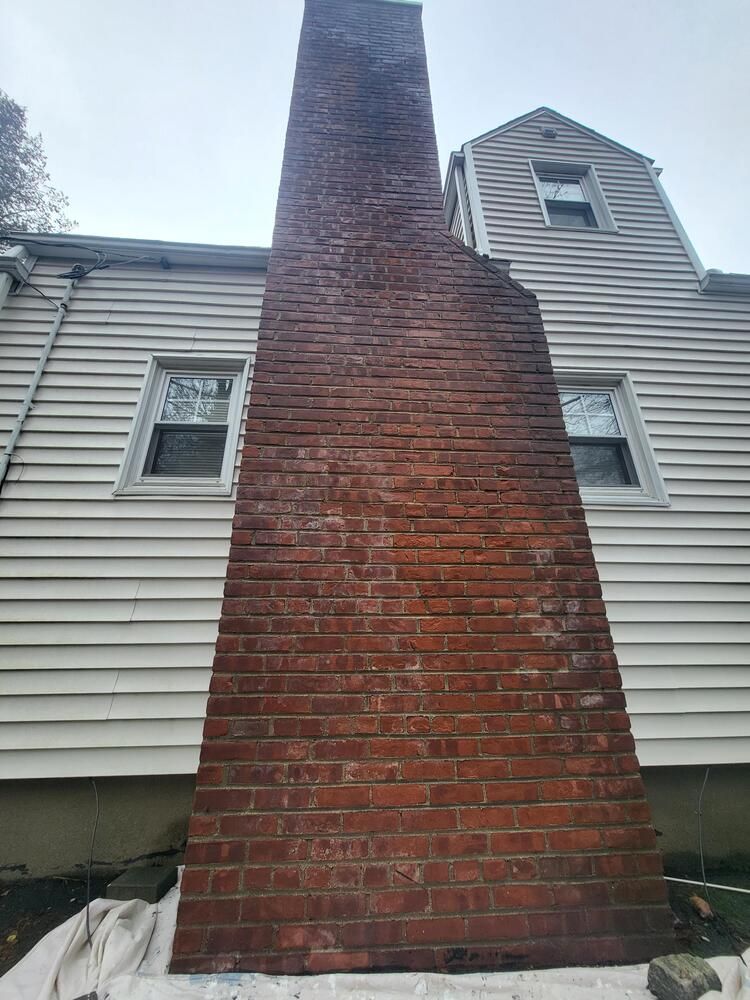 Tall red brick chimney on a white-sided house exterior with dormer windows