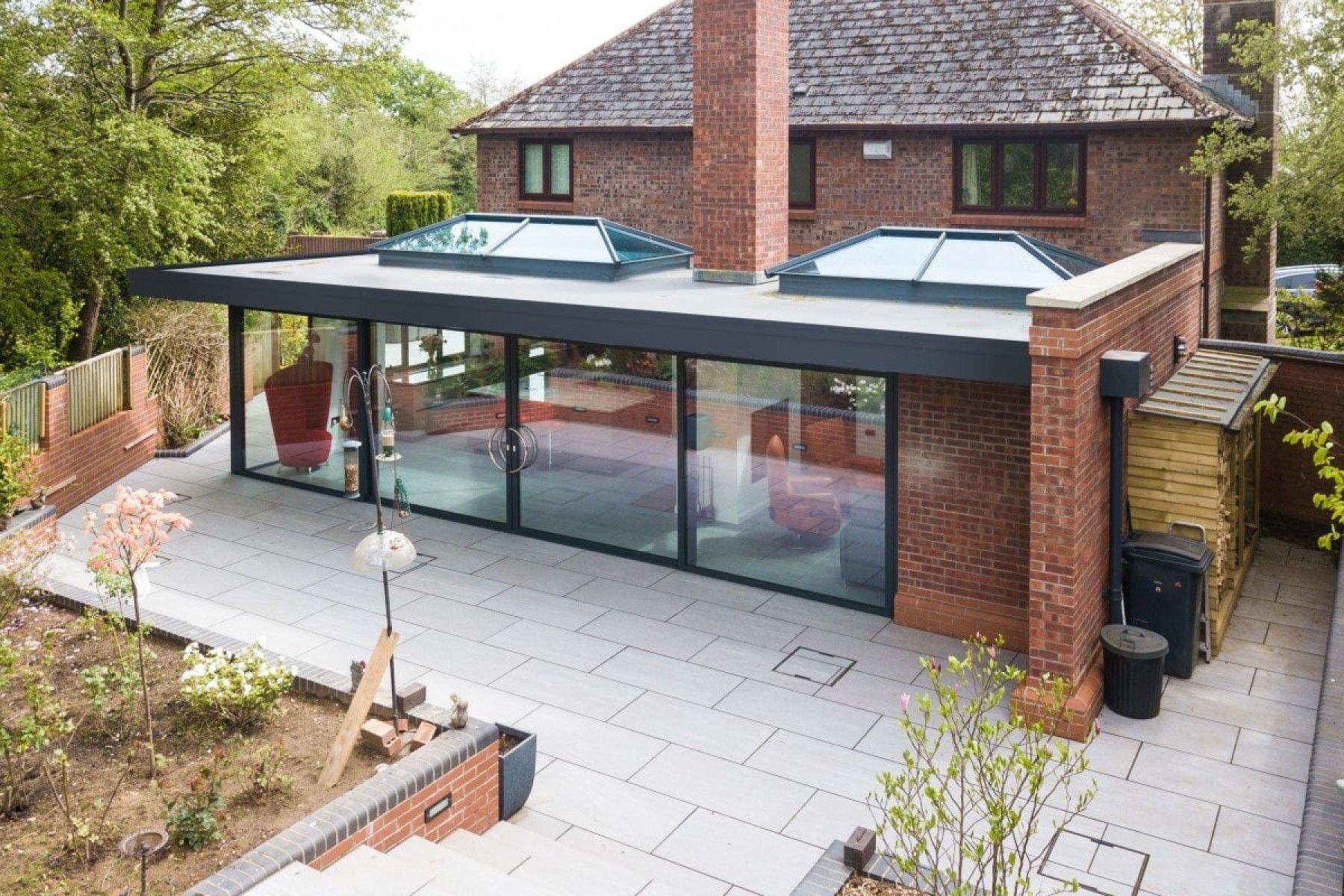 Modern brick house with a large glass conservatory and paved patio, viewed from above