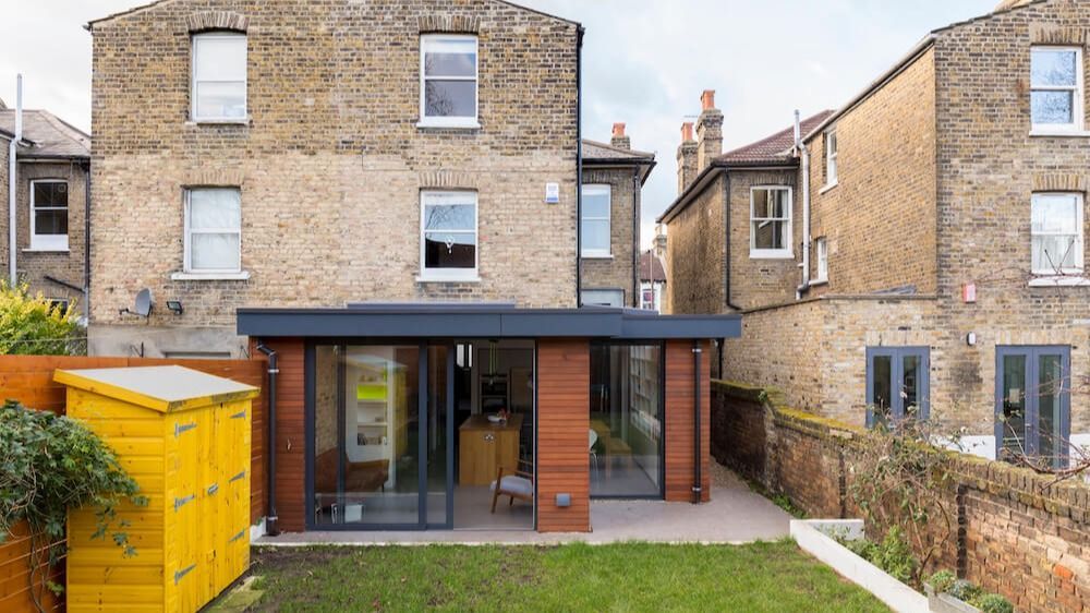 Backyard patio with glass doors on a brick house, lawn, yellow storage bin, and neighboring homes