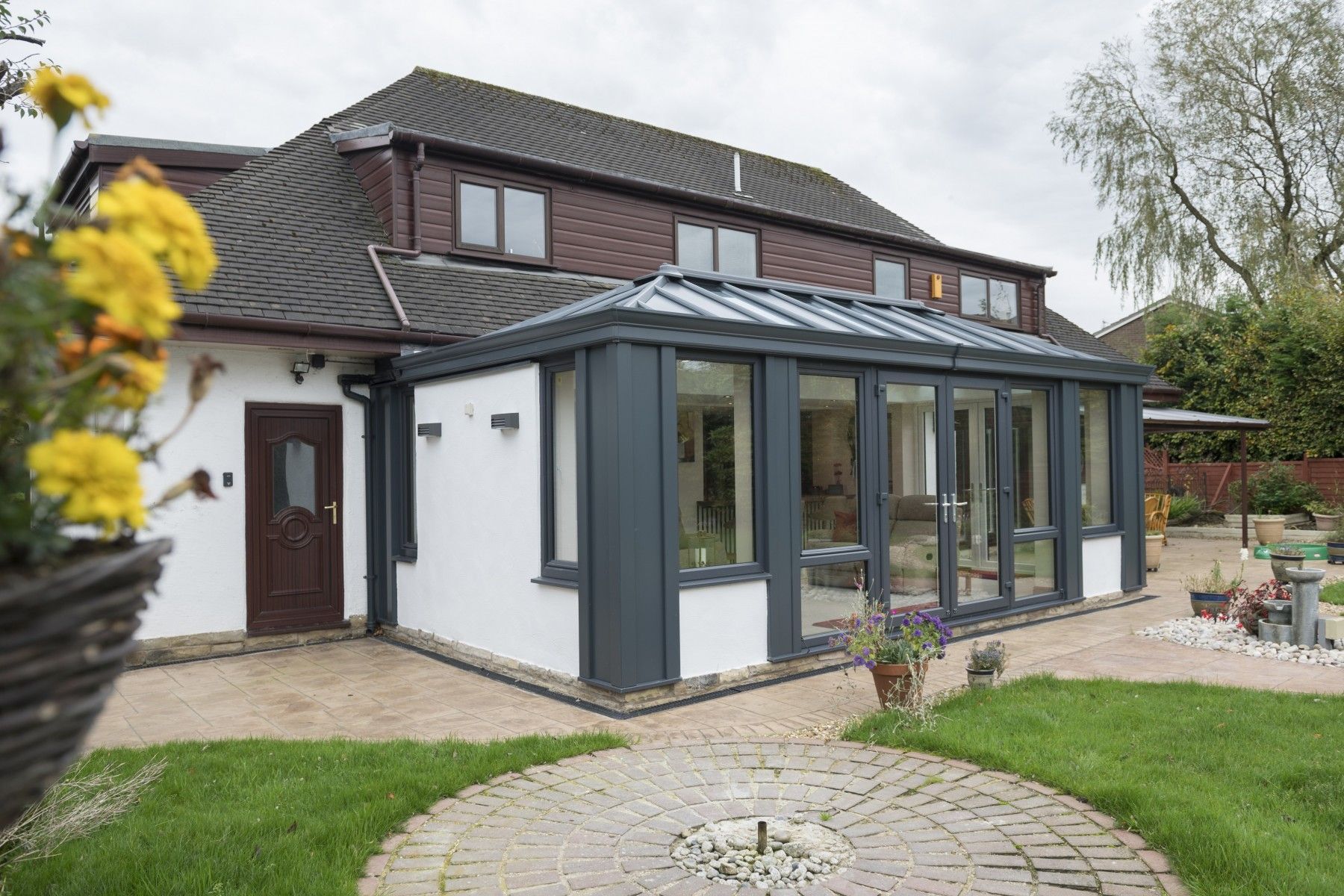 Modern house with a glass sunroom, white walls, dark roof, and curved stone path in a garden
