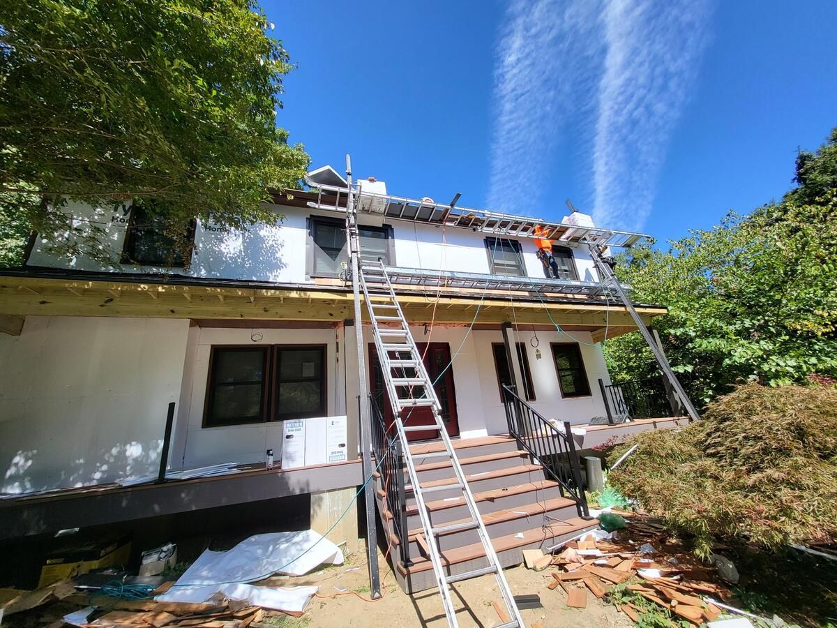 House exterior with ladder to roof, surrounded by trees under a blue sky