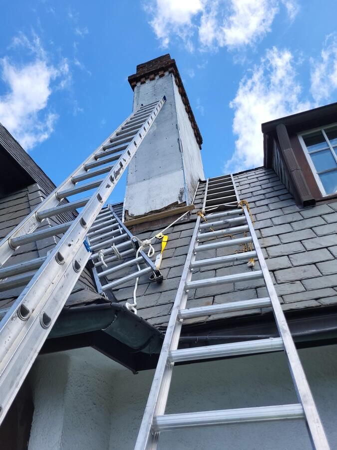 Two ladders leaning against a house chimney under a blue sky with clouds