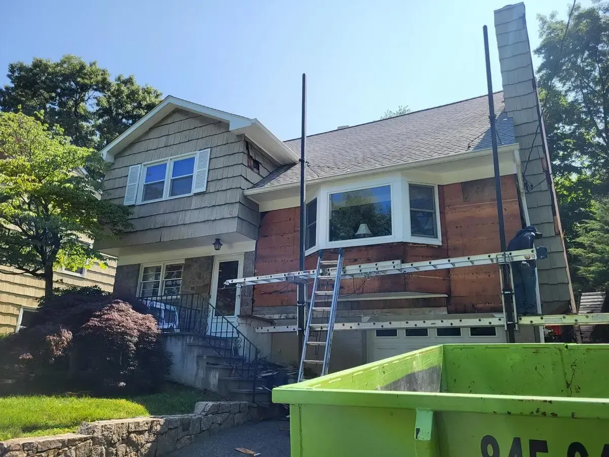 House exterior with ladders and a green dumpster in front, suggesting ongoing home repairs