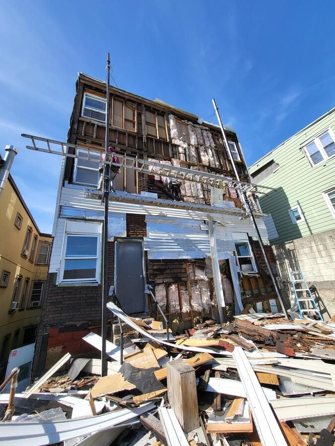 Partially collapsed house with damaged exterior and debris piled in front under a blue sky