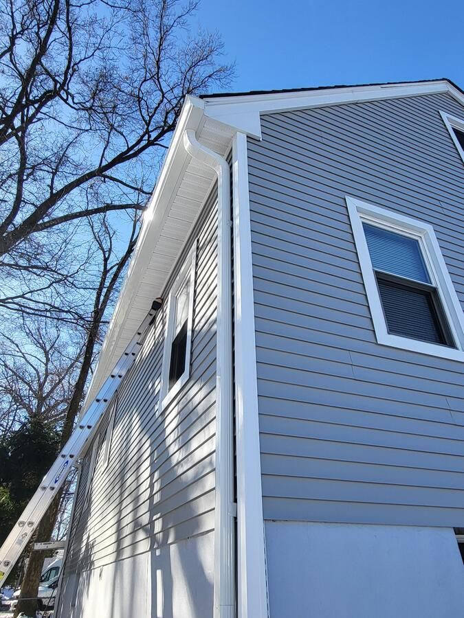 Side of a gray house with white trim and windows, viewed from below beside leafless trees