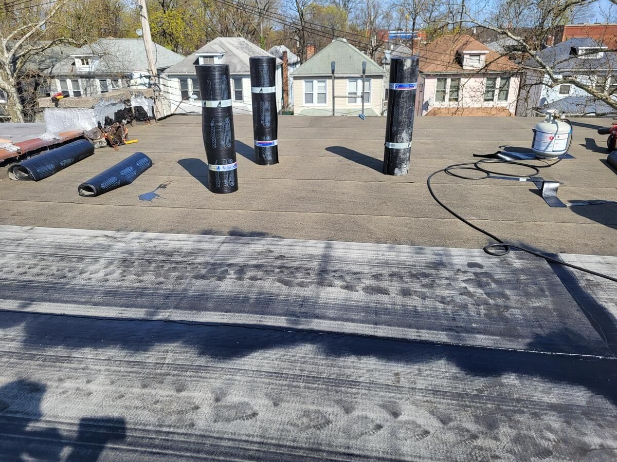 Rooftop with several black vent stacks and a worker on the right, with houses in the background