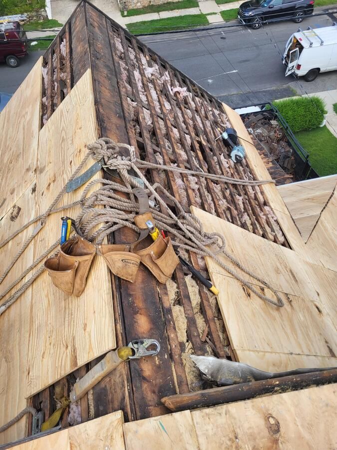 Roof repair with exposed wood framing, tarps, and ropes, viewed from above above a street.