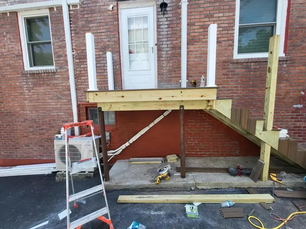 Wooden porch ramp under construction beside a brick building, with tools and ladder nearby