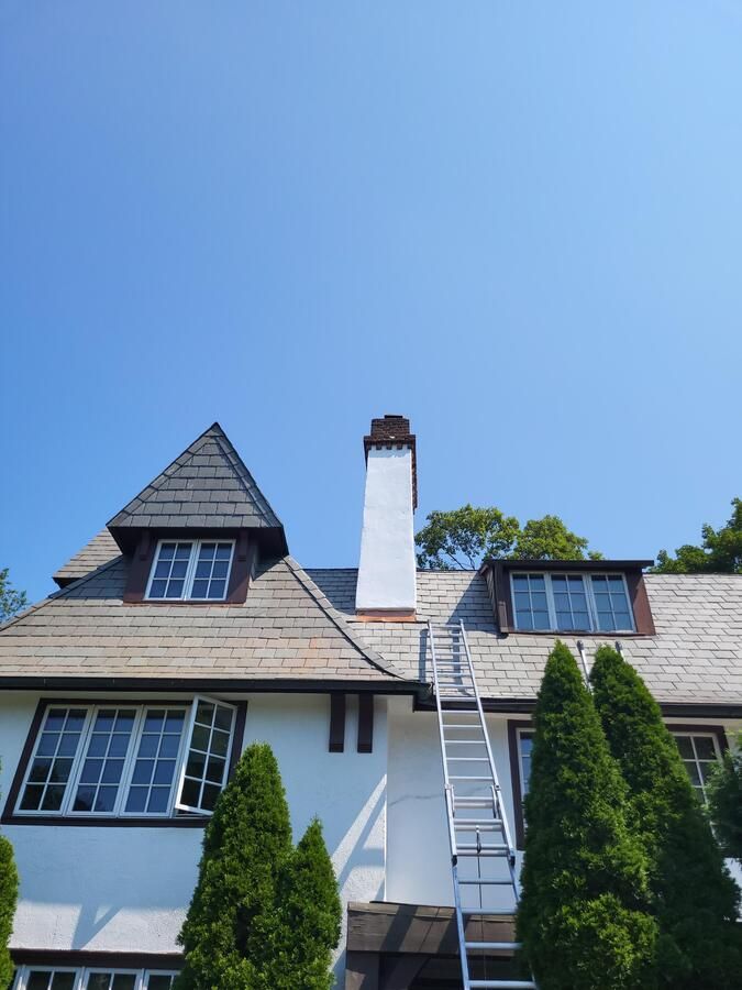 White house with steep roof, chimney, and ladder under a clear blue sky.