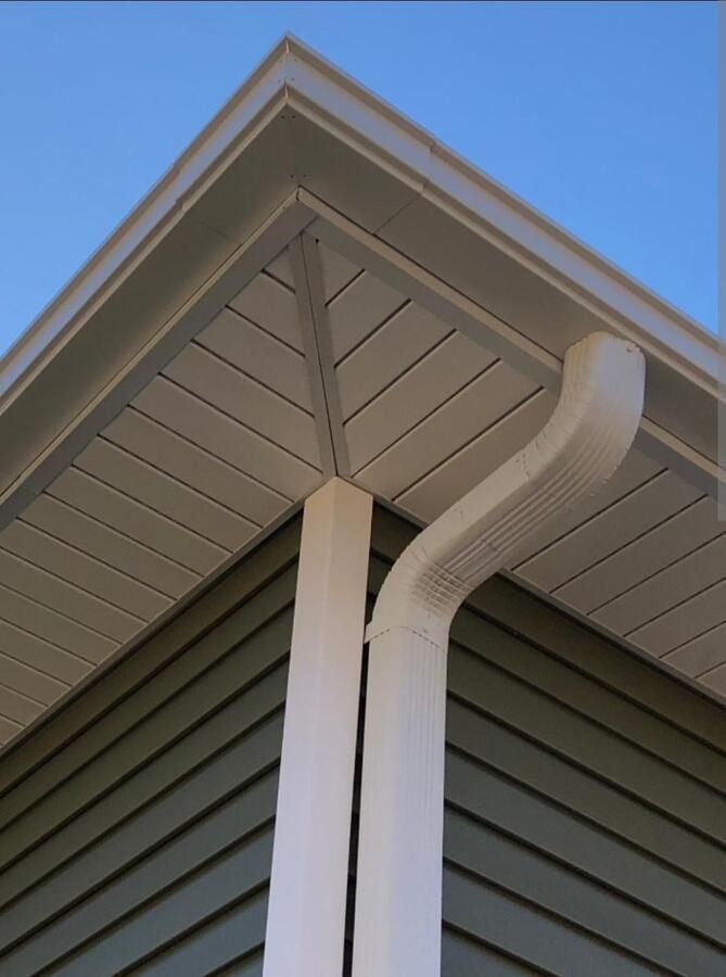 Close-up of house roof eaves with white gutter and downspout against blue sky