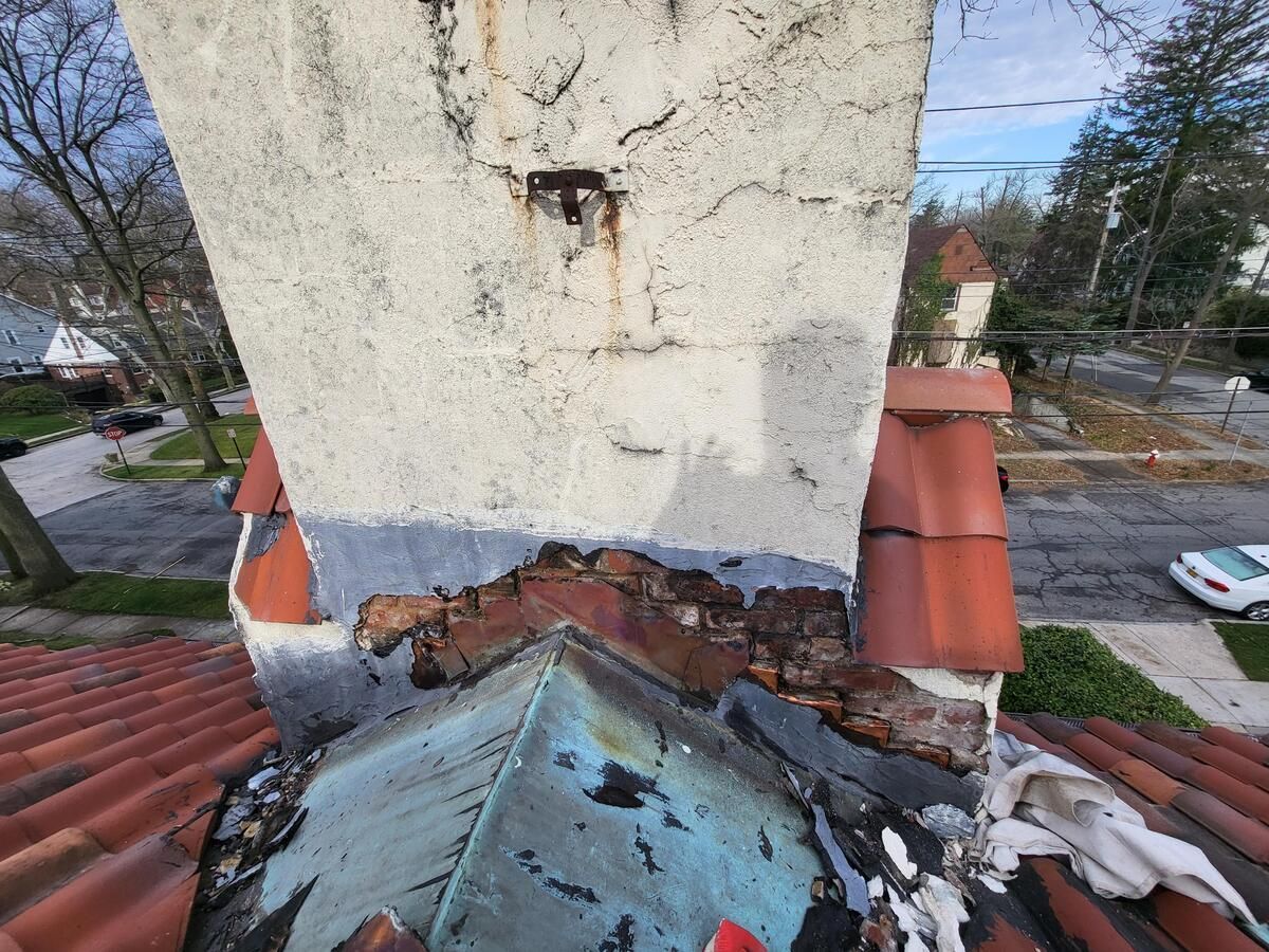 Damaged chimney above a red-tiled roof, with peeling plaster and broken masonry.