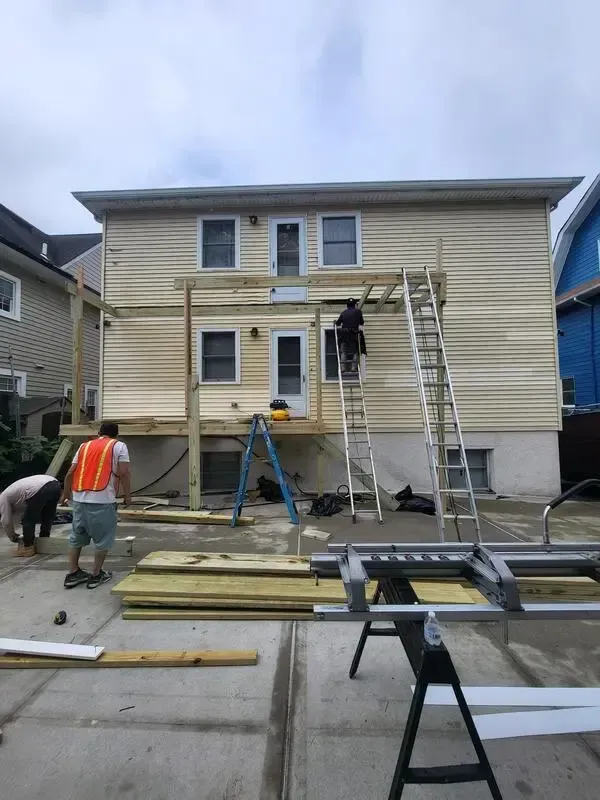 Construction workers on ladders painting a two-story house exterior during renovation.