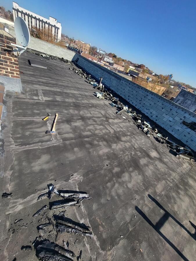 Rooftop covered in black roofing material, seen at a slanted angle under a clear blue sky.