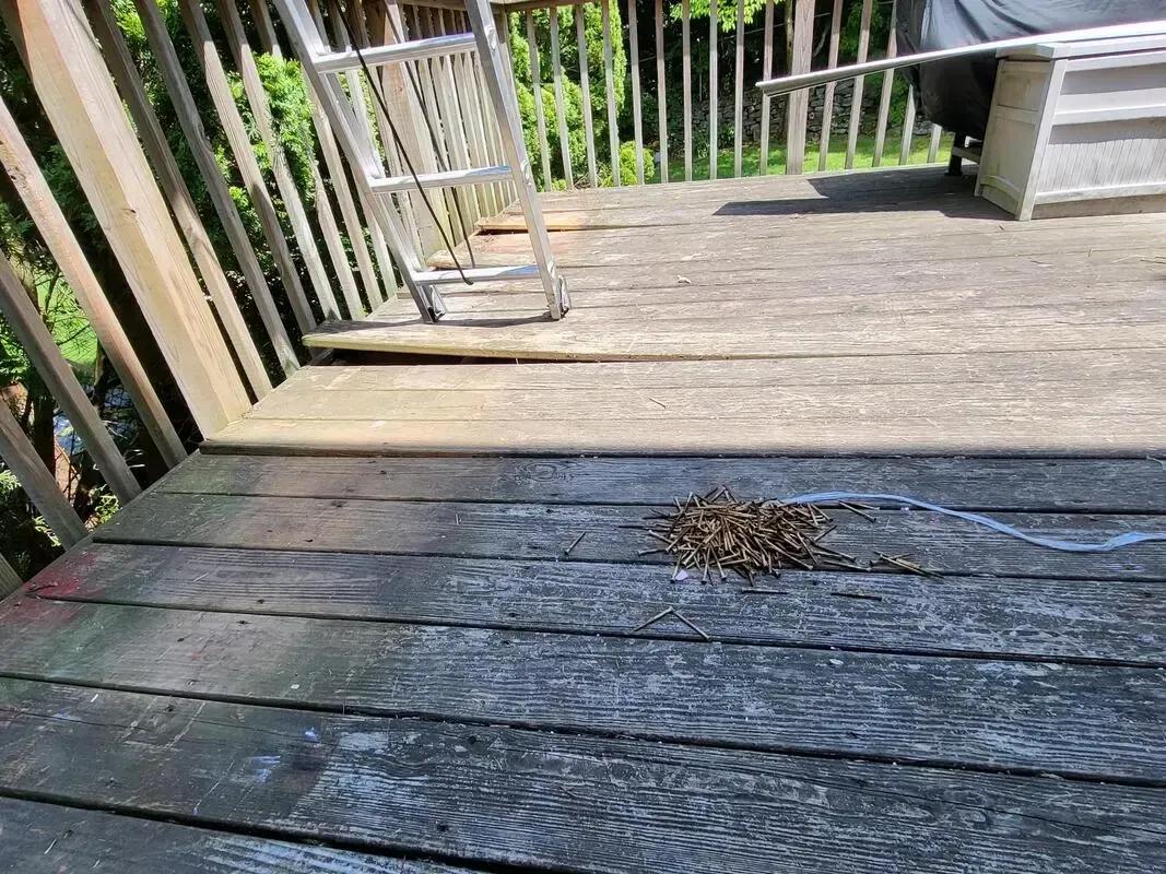Weathered wooden deck with a small pile of leaves and railings in the background