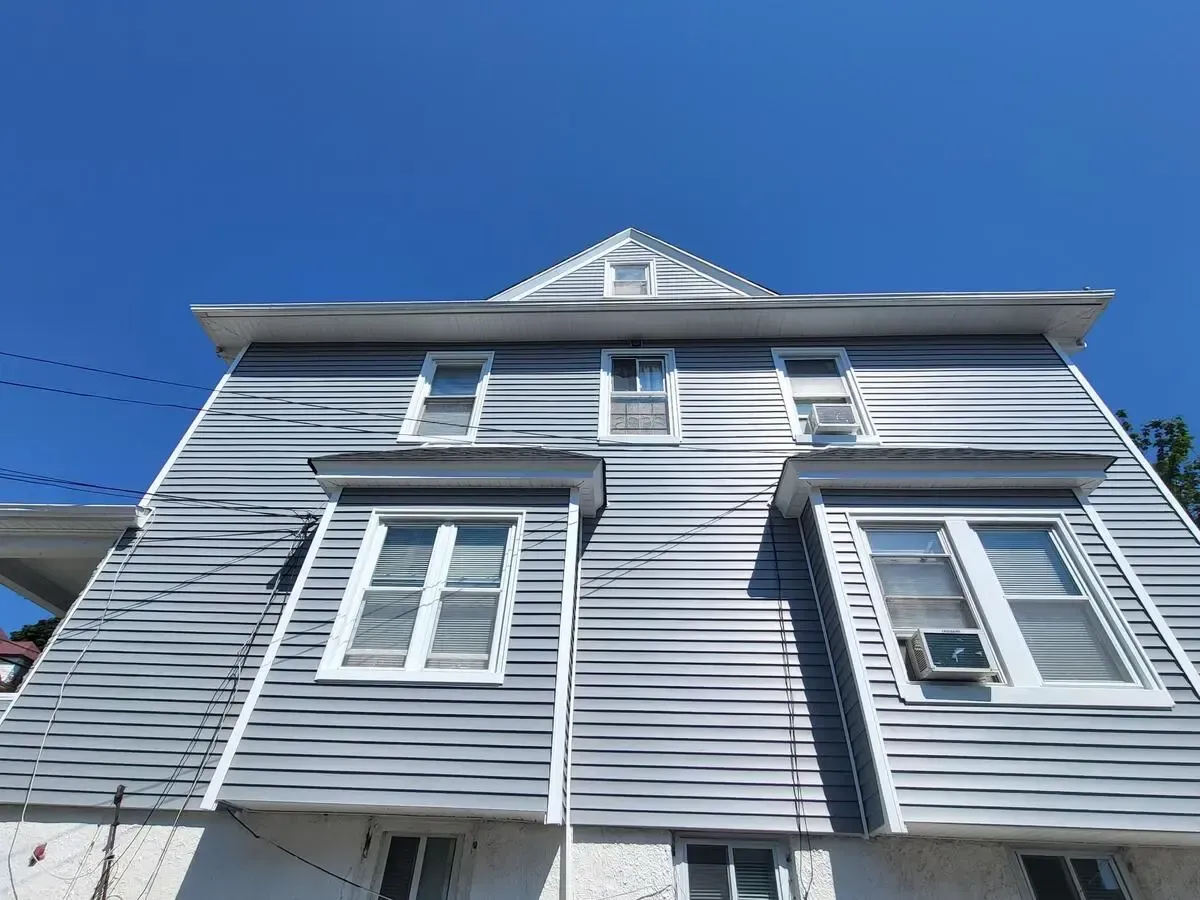 Low-angle view of a gray house with white-trimmed windows against a clear blue sky