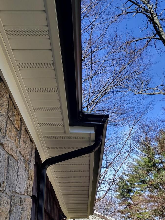 House roof gutter beside stone wall under blue sky