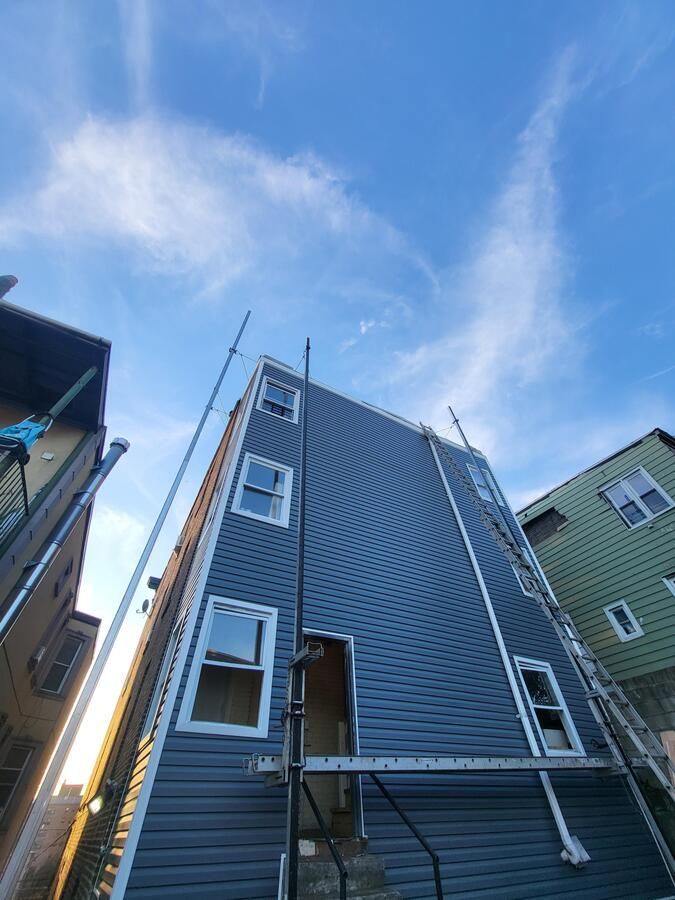 Tall blue-gray house with white-trimmed windows viewed from below against a blue sky