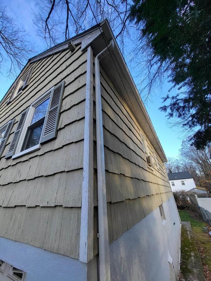 Corner of a beige clapboard house with blue shutters and white foundation under a blue sky