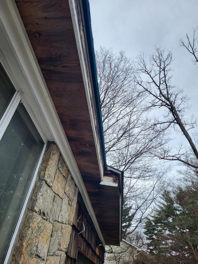 Close-up of a stone house exterior with roof eaves and bare trees against a cloudy winter sky