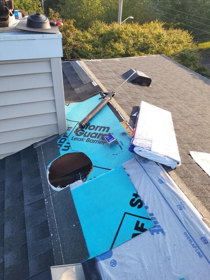 Roof with exposed blue and white underlayment around chimney and vents, showing roof repair work