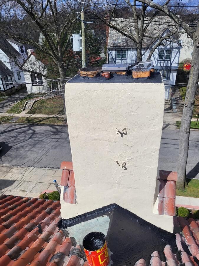 Rooftop chimney with white stucco flue, black cap, and red roof tiles, overlooking a residential street.