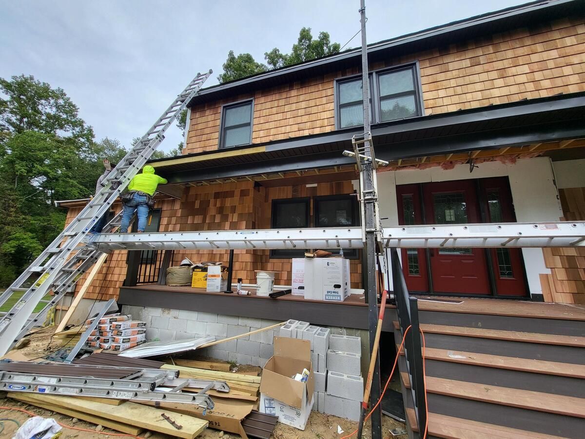 Workers on scaffolding renovating a two-story house with exposed siding and roof work