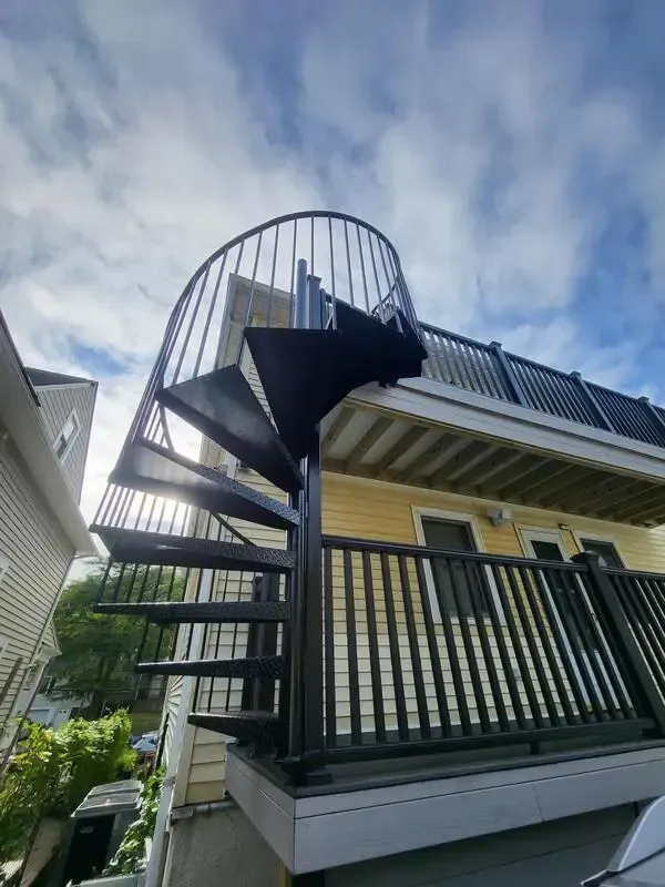 Exterior of a house with a black spiral staircase and balcony under a cloudy sky