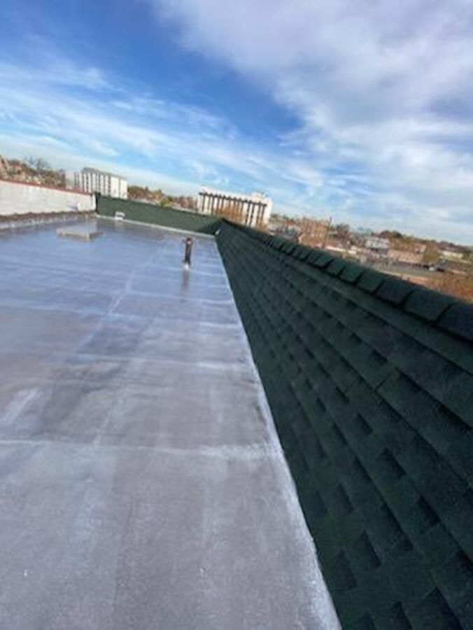 Flat rooftop with a reflective surface, dark green parapet, and blue sky with clouds.