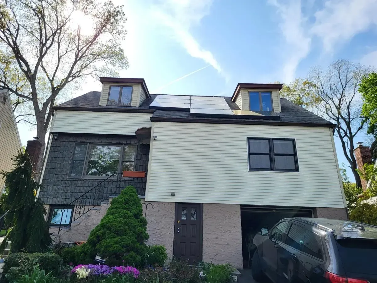 Two-story house with dark roof, light siding, trees, and a black car parked in front