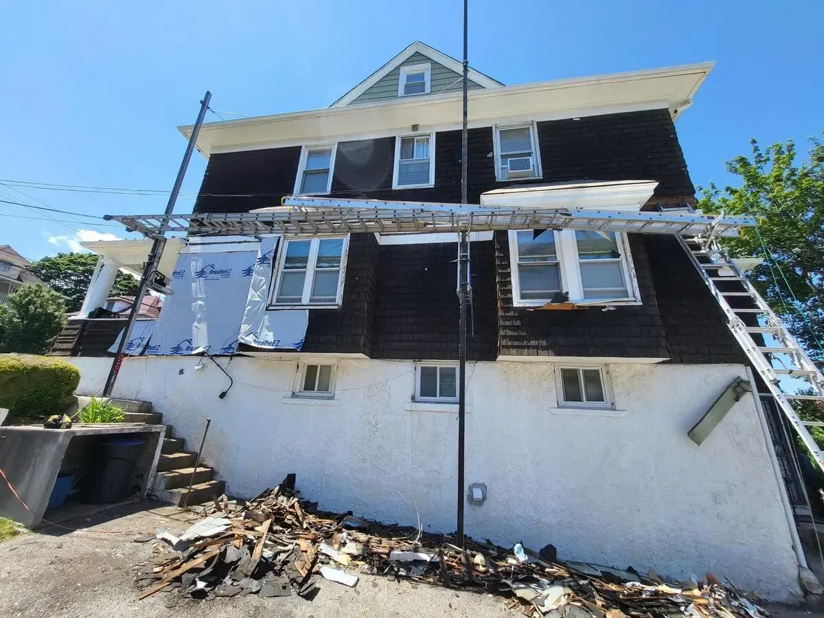Two-story house with exterior repair work, ladders, scaffolding, and debris in front.