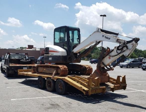 Tracked excavator loaded on a flatbed trailer in a parking lot under a cloudy sky