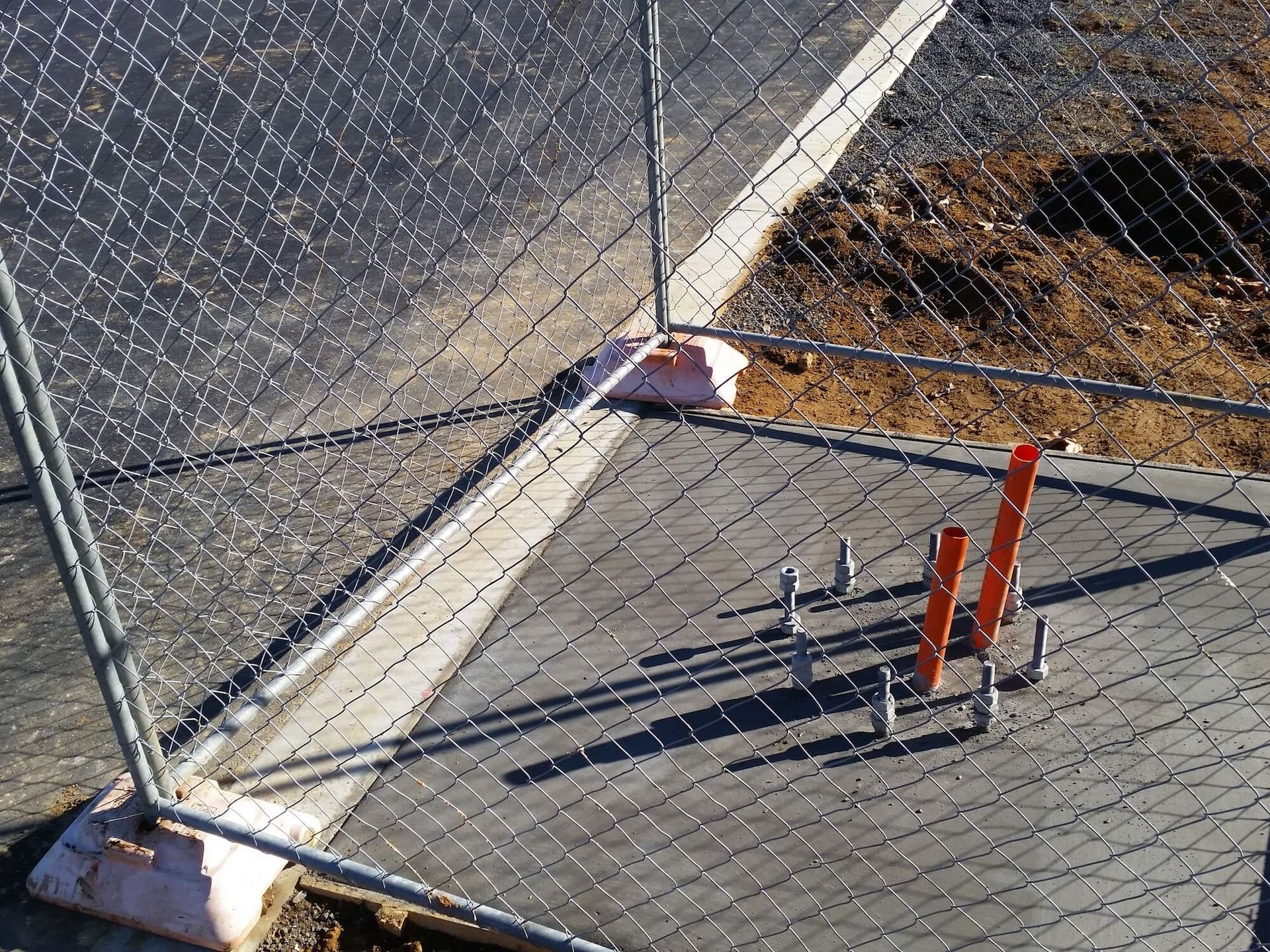 Chain link fence sections secured by concrete blocks; orange construction stakes visible.