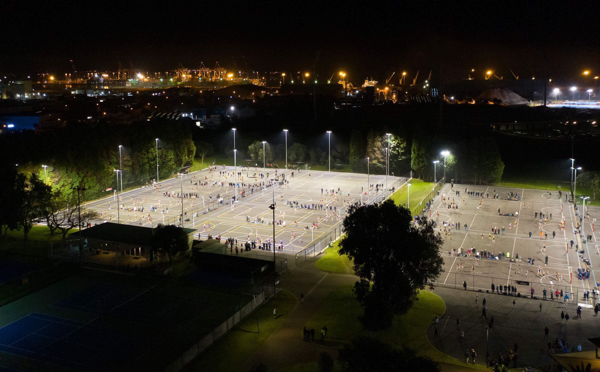 Night aerial view of a crowded outdoor space lit by bright streetlights; many people are visible.