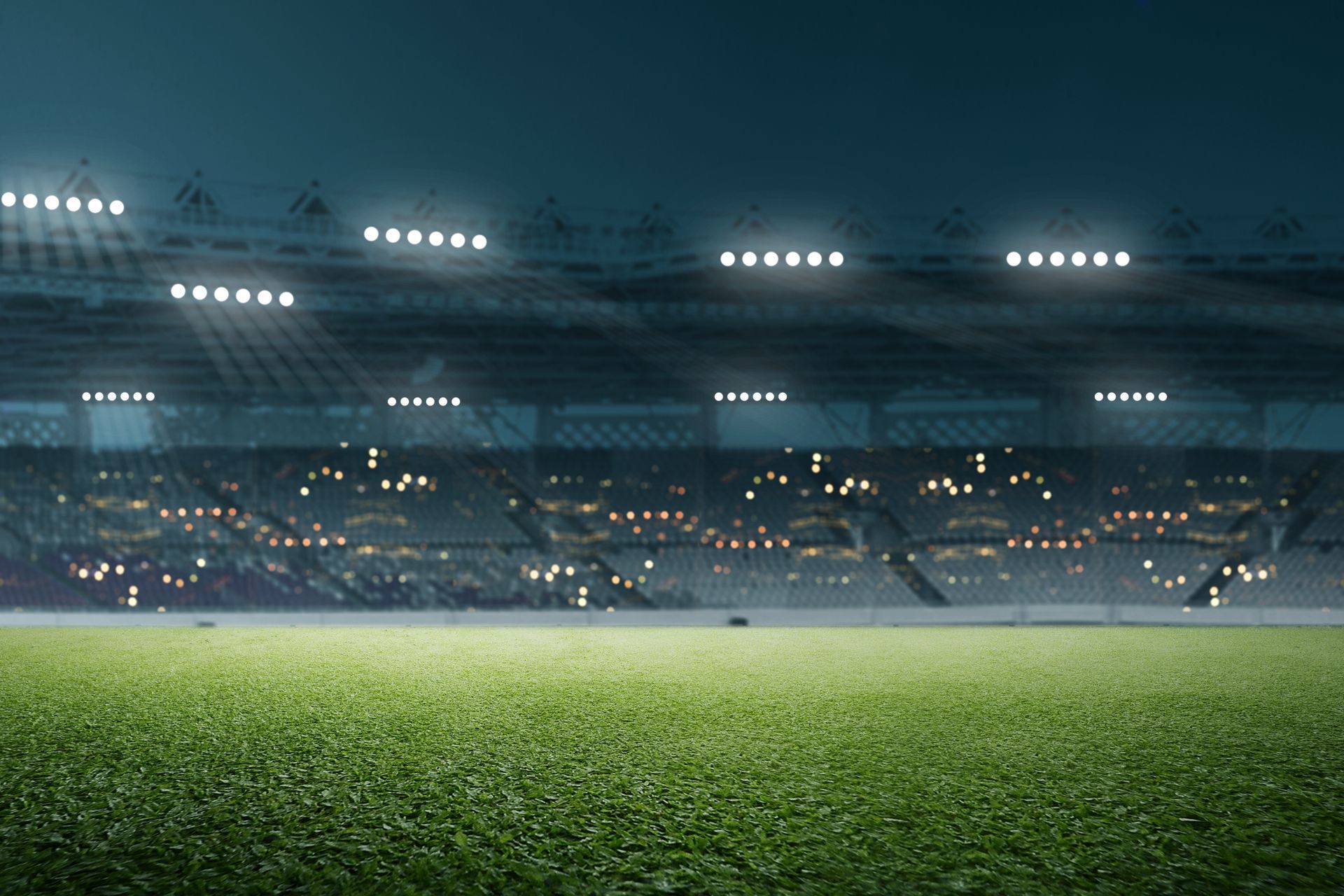 A low-angle shot of a field in a large sports stadium at night with bright floodlights.
