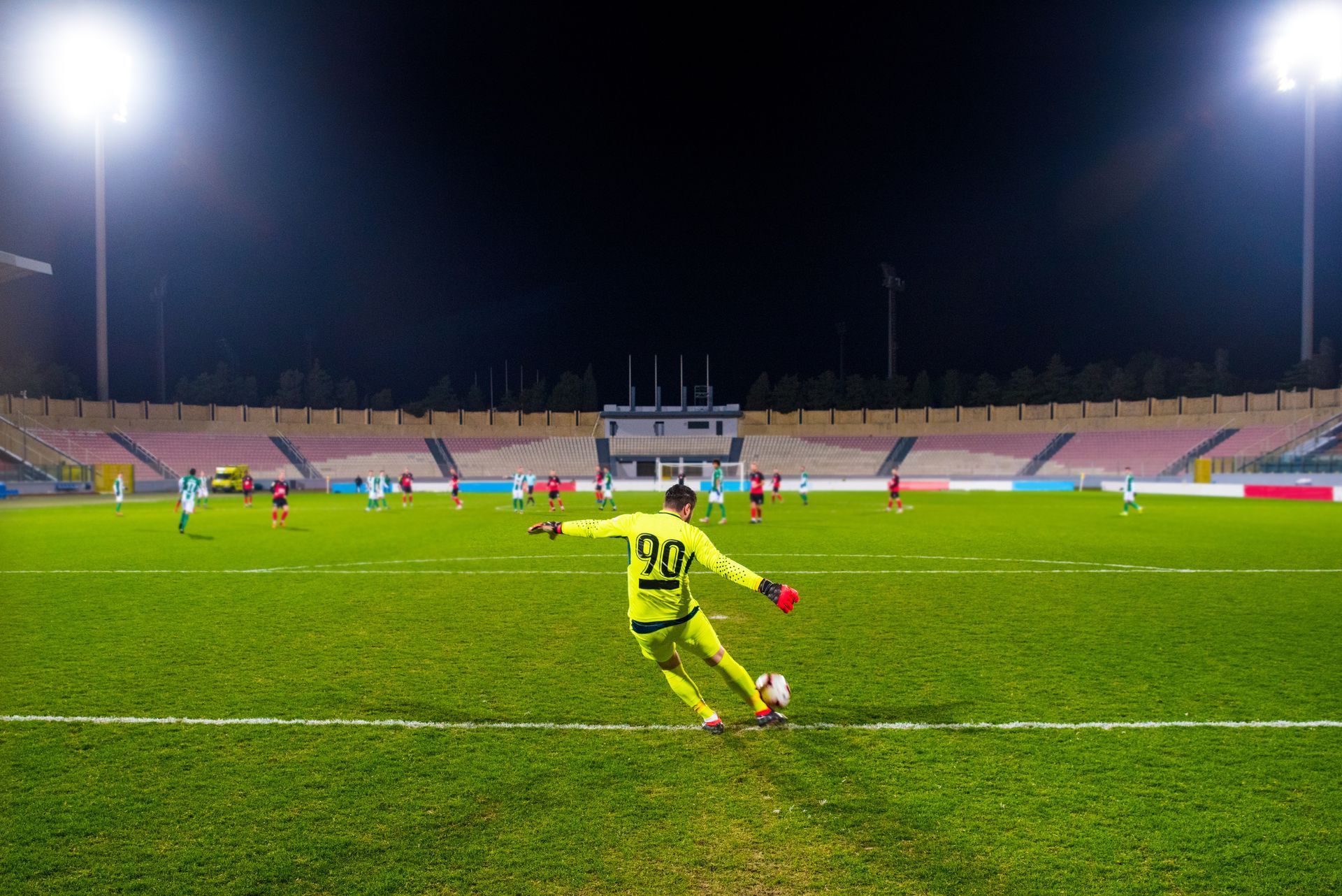 Goalkeeper kicking the ball at a stadium illuminated by floodlights. Goalkeeper kicking the ball at a stadium illuminated by floodlights.