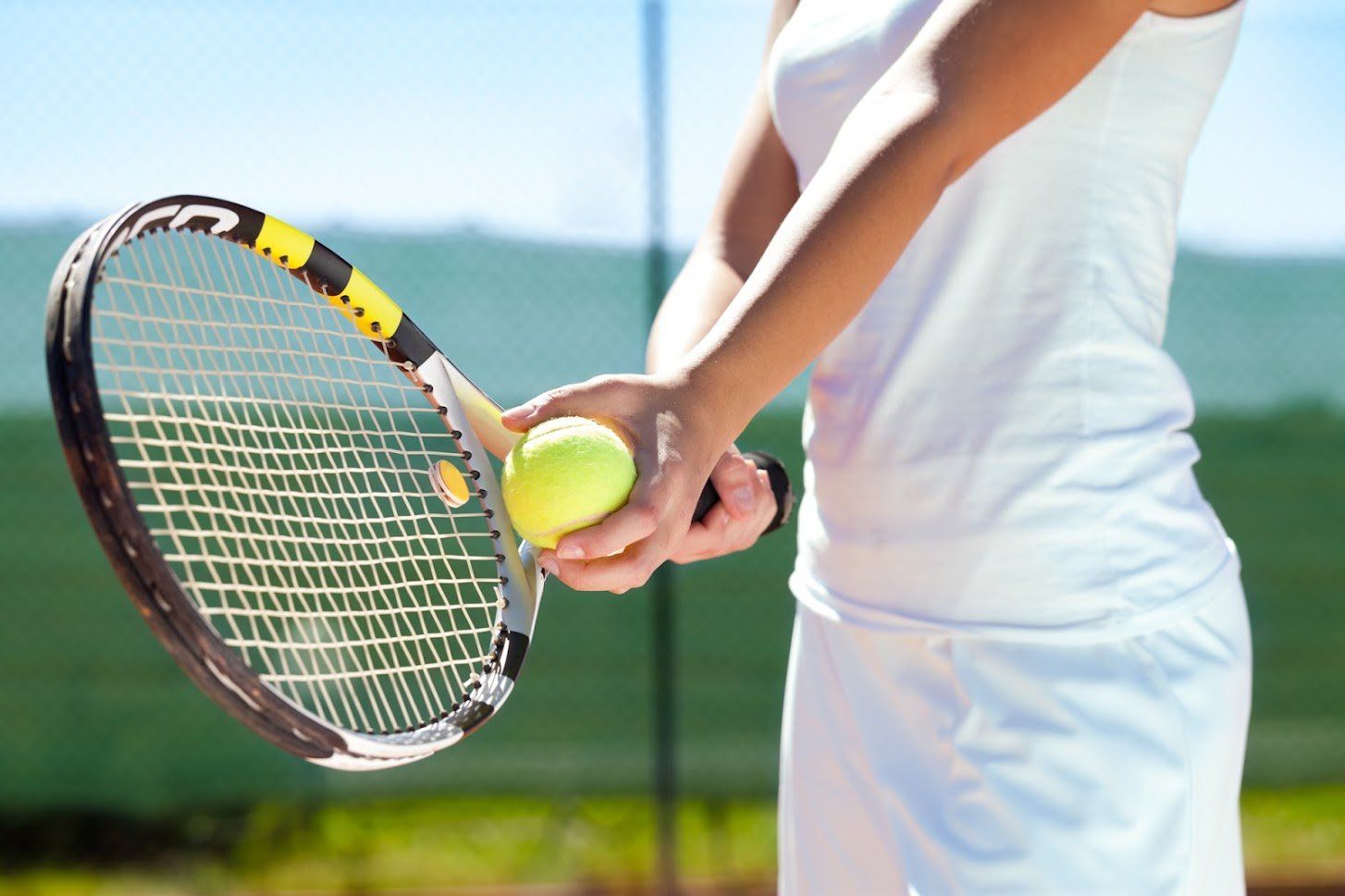 Tennis player in white attire holding a racquet and a yellow tennis ball on a court.