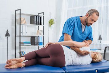 Chiropractor adjusting patient's back on a table in a bright room.