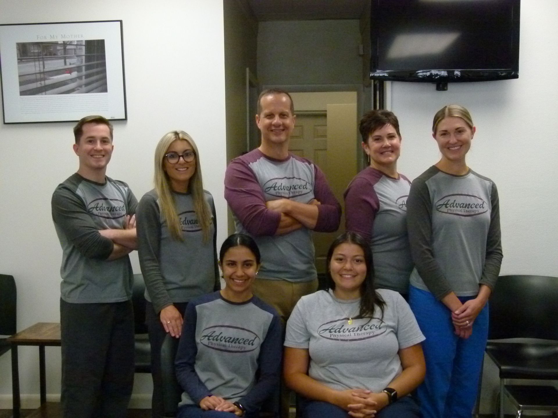 A group of eight people wearing matching gray and maroon shirts pose for a photo in an office waiting area.