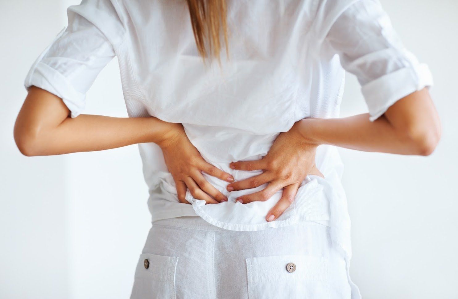 Person in a white shirt and pants holding their lower back due to pain.