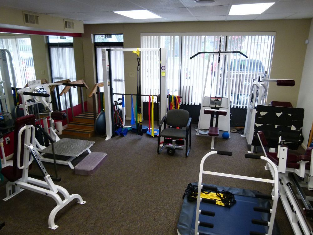 An indoor physical therapy or fitness studio containing various exercise equipment, including weight machines and a chair.